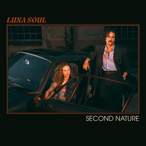 Text: "LUNA SOUL" oben links, "SECOND NATURE" unten rechts. Ein Mann lehnt an einem Auto; eine Frau sitzt darin. Elegante Kleidung.