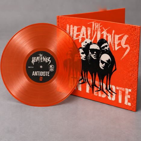 Text: "The Headlines", "Antidote". Eine transparente orangefarbene Vinylplatte lehnt an einem Cover mit Köpfen.