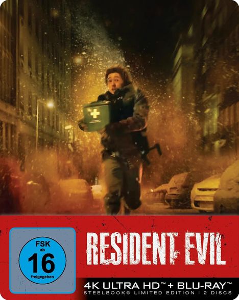 "Resident Evil" Text. FSK 16. Person mit Erste-Hilfe-Kasten rennt durch staubige Stadtstraße, Explosionen im Hintergrund.