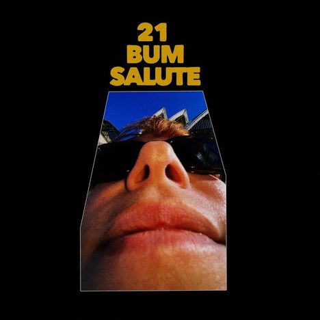 Text: "21 BUM SALUTE". Nahaufnahme eines Gesichts mit Sonnenbrille, im Hintergrund moderne Architektur.