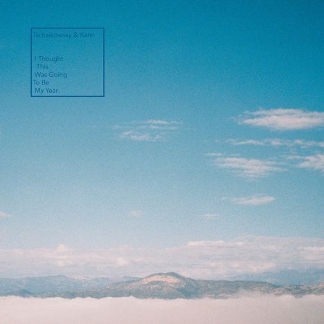 „Tschai­kowsky & Kann. I Thought This Was Going To Be My Year“ steht links. Ein wolkiger Himmel über Bergen.