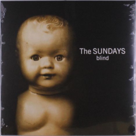 „The SUNDAYS blind“ steht neben einem antiken Puppenkopf mit großen Augen, in sepia gehalten.