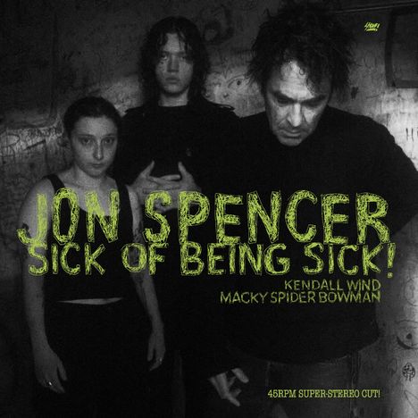 Schwarz-weiß Foto von drei Personen vor einer Wand mit Kritzeleien. Text: "Jon Spencer Sick of Being Sick!".