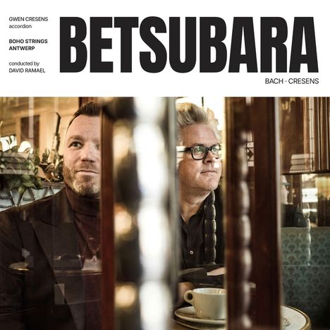 Text: BETSUBARA. Personen in einem Café; links Mann mit Bart, rechts Mann mit Brille, entspannte Atmosphäre.