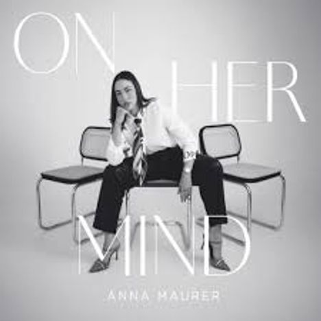 "ON HER MIND" und "ANNA MAURER". Frau sitzt lässig auf Stühlen, trägt Anzug und Krawatte. 