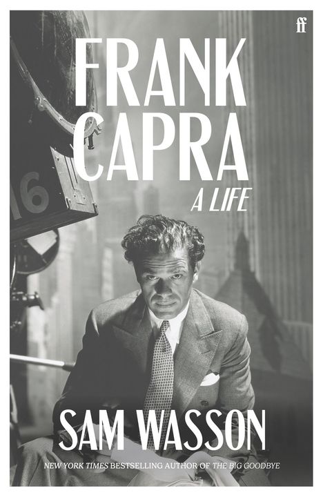 "FRANK CAPRA: A LIFE. SAM WASSON. Ein Mann in Anzug mit ernster Miene sitzt, Kameratechnik sichtbar im Hintergrund."