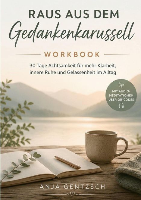 „Raus aus dem Gedankenkarussell“, Achtsamkeits-Workbook. Offenes Notizbuch, Stift, Tasse auf Holztisch, Ausblick auf Berge.