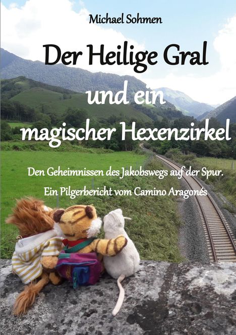 Titel: Der Heilige Gral und ein magischer Hexenzirkel. Drei Kuscheltiere vor einer grünen, bergigen Landschaft mit Bahngleisen.