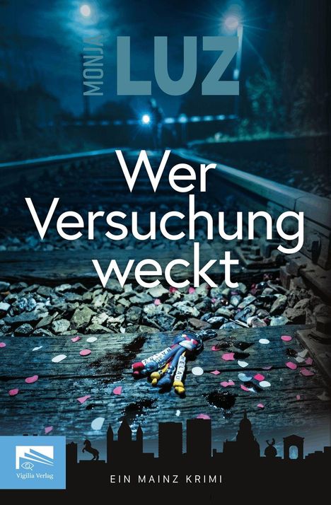 Text: "Wer Versuchung weckt. Ein Mainz Krimi." Darunter Gleise mit Konfetti und einem kleinen Seil mit Anhängern.