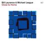 Text: "Bill Laurance & Michael League, Close to Home". Illustration: Blaue Quadrate mit dunklem zentralen Quadrat.