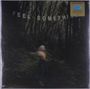 Text: "FEEL SOMETHING". Unscharfe Person auf Waldweg, umgeben von Bäumen, dunkle Atmosphäre.