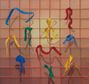 Bunte Schleifen (blau, grün, rot, gelb) hängen an einem Gitternetz, lassen ihre Schatten auf einem rosa Hintergrund fallen.