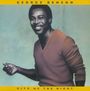 "George Benson, Give Me the Night." Ein lächelnder Mann in einem orangefarbenen Pullover vor blassem Hintergrund.