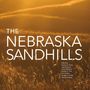 "The Nebraska Sandhills" in großer Schrift, darunter Herausgebernamen. Im Hintergrund Sonnenuntergang über einer Graslandschaft.
