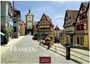 „Franken“ in großer Schrift. Kopfsteinpflasterstraße mit Fachwerkhäusern, Turm im Hintergrund, blauer Himmel.