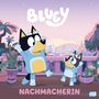 Text: "Bluey" und "Nachmacherin". Illustration zweier fröhlicher Hunde in blauen Outfits auf einer Terrasse mit Stadt im Hintergrund.