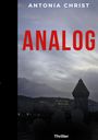 Text: „ANTONIA CHRIST“, „ANALOG“, „Thriller“. Ein trüber Himmel über einer Stadt mit beleuchtetem Gebäude, Silhouetten im Vordergrund.