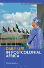 „Daily Life in Postcolonial Africa“ – Toyin Falola. Ein Mann in traditioneller Kleidung vor Flaggen und Gebäuden.