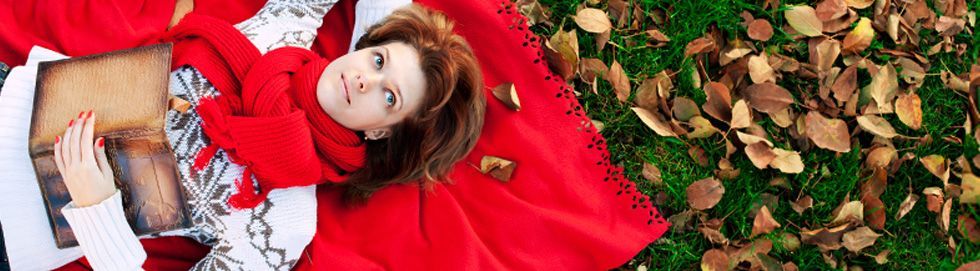 Frau liegt auf einer roten Decke im Laub und hält ein Buch